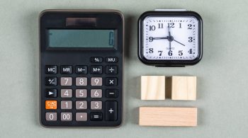 Time management and accounting concept with magnifier, wooden blocks, calculator and watch on gray background top view. horizontal image